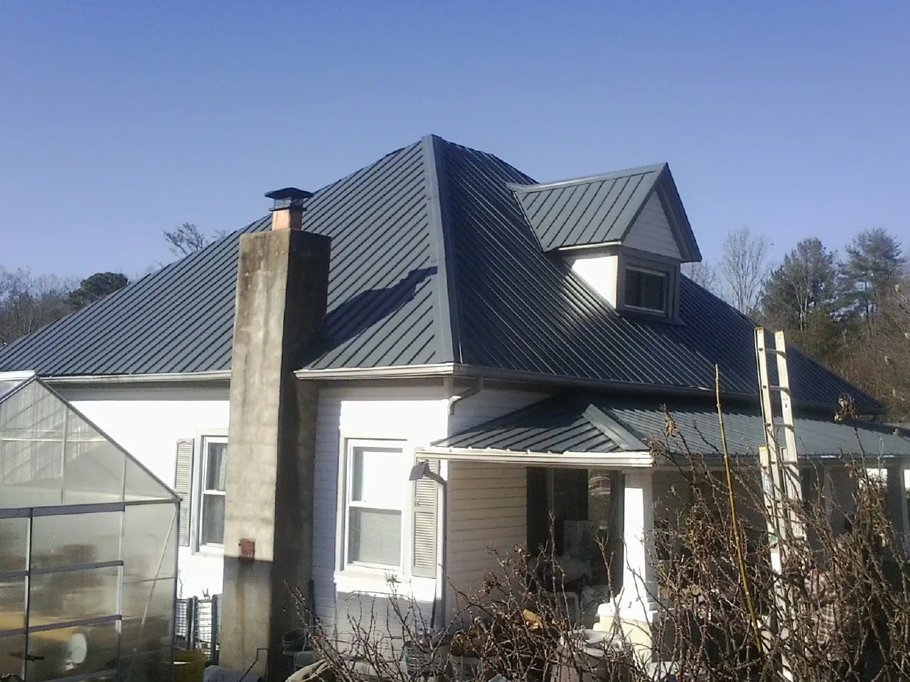 Dark blue standing seam metal roof on a white farmhouse with dormer — Slate & Tile Roof Repair by Roofing Brothers in Mc Clellanville