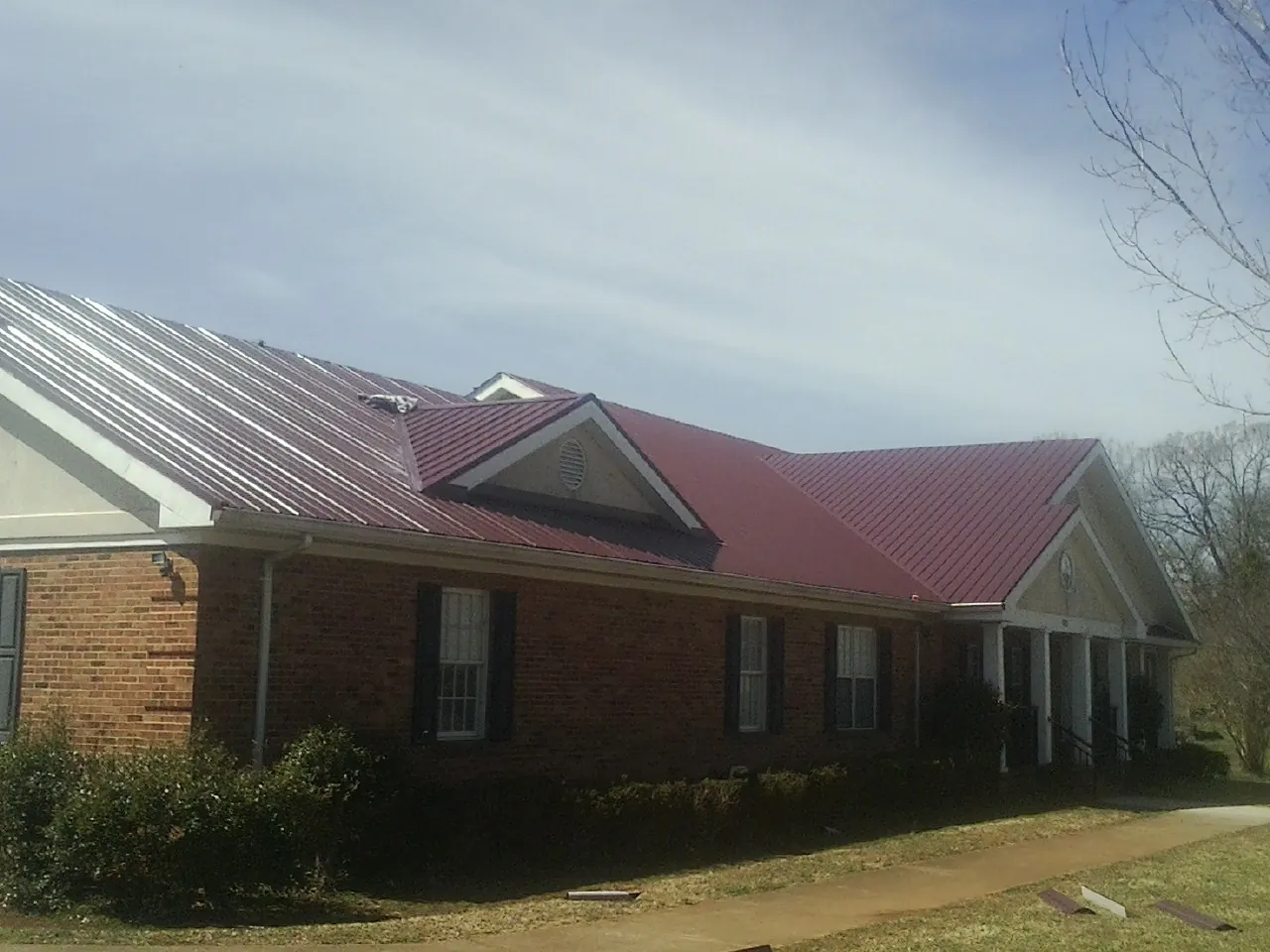 Red metal roof with gabled entries on a long brick building, from a Hail Damage Roof Repair job in Mc Clellanville