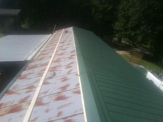 Old rusted panels beside newly installed green metal roofing — Wind Damage Roof Repair by Roofing Brothers in Mc Clellanville