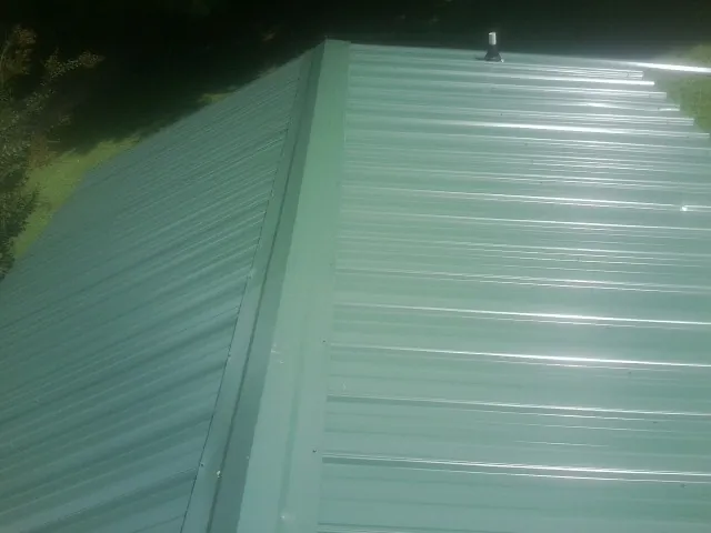 New green metal panels meeting at the ridge of a roof — Flat Roof Repair work by our crew in Mc Clellanville