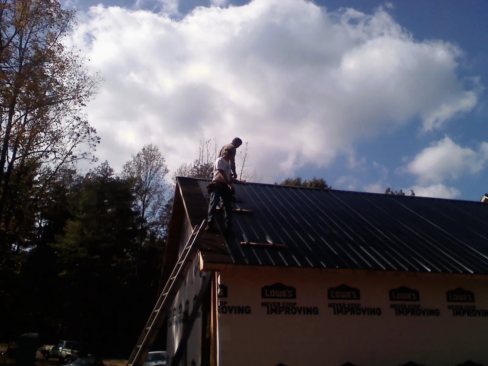 Roofer fastening dark metal panels high against a cloudy sky, from a Roof Inspection job in Mc Clellanville