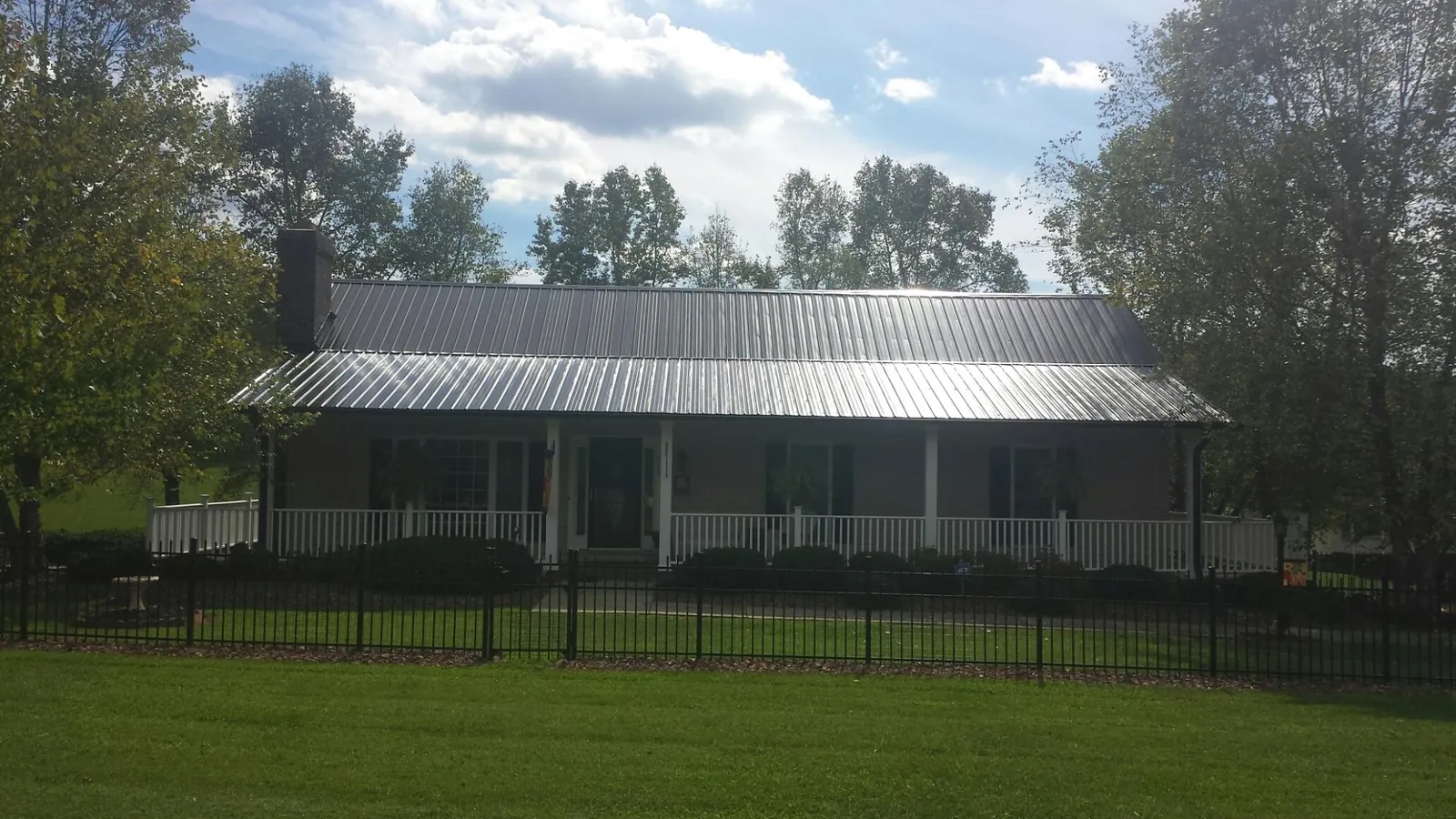 Gray metal roof on a brick ranch with a full width front porch — Gutter Guard Installation work by our crew in Mc Clellanville