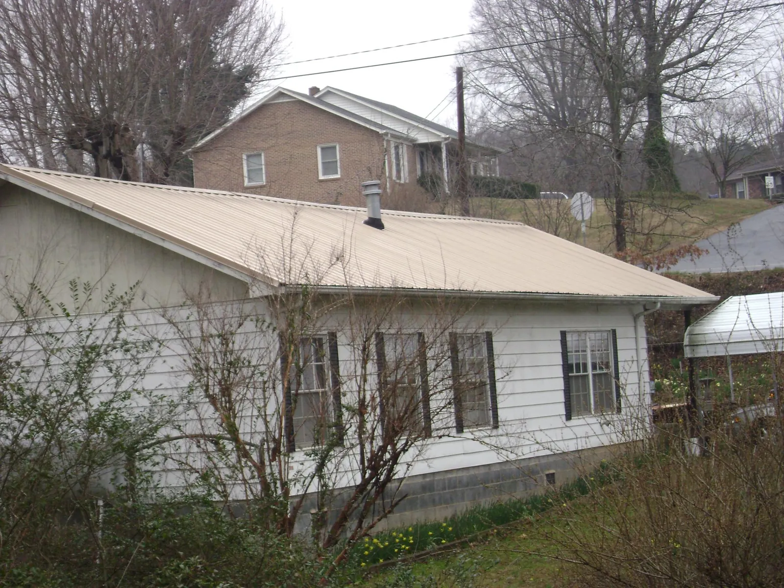 Tan metal roof on a white sided house set into a hillside — Commercial Roofing by Roofing Brothers in Mc Clellanville